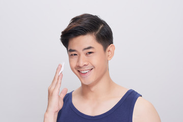 Handsome man cleaning face skin with batting cotton pads over gray background and looking at camera