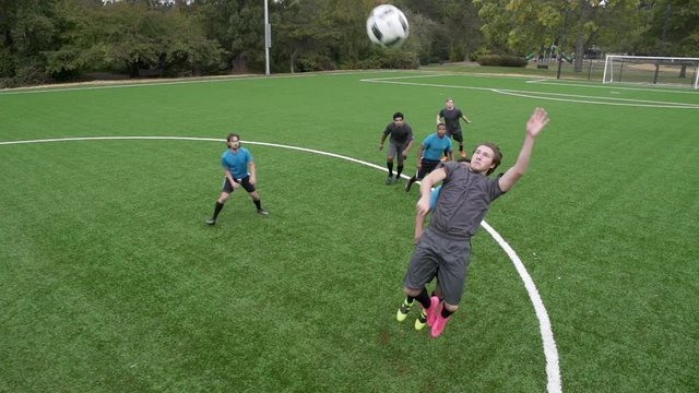 Male soccer players on soccer pitch watching ball.