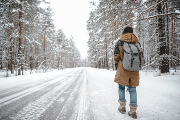 Backpacker girl walk near the road in snow forest