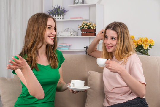 Two young attractive women sit on a sofa in the room and I talk about something.