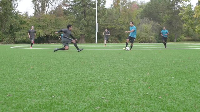 Male soccer players playing soccer with one man injuring himself.
