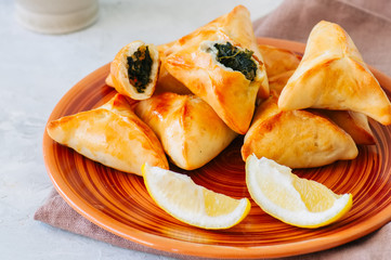 Arabic and middle eastern food concept. Fatayer sabanekh - traditional arabic spinach triangle hand pies dates and tea on a white stone background.