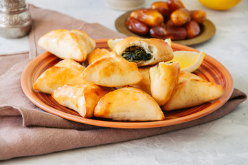Arabic and middle eastern food concept. Fatayer sabanekh - traditional arabic spinach triangle hand pies dates and tea on a white stone background.