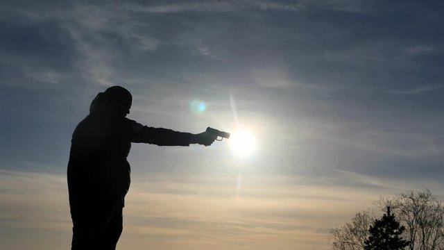 Silhouette of man training to shoot with pistol outdoors