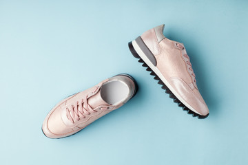 Pastel pink female sneakers on blue background. Flat lay, top view minimal background.