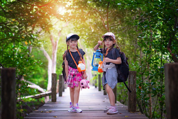 twin kids walking-in wooden bridge of forest jungle for joining field trip for replenish nature life education, looking to see at dark forward find firerfly bug in the night with lamp lantern