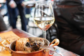 Florence, Tuscany / Italy. - April 21, 2018.  aperitif a glass of white wine and dark olives with pepper and bread, snacks are served in a copper pan on a wooden table.