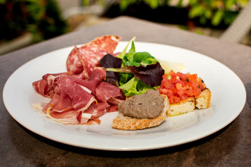 lorence, Tuscany/Italy - April 21, 2018. traditional Italian appetizers "antipasti": salami, dried meat (prosciutto), toast with tomatoes and olive oil (crostini), toast with pate, lettuce.