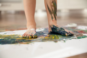 The child paints on the paper with his feet