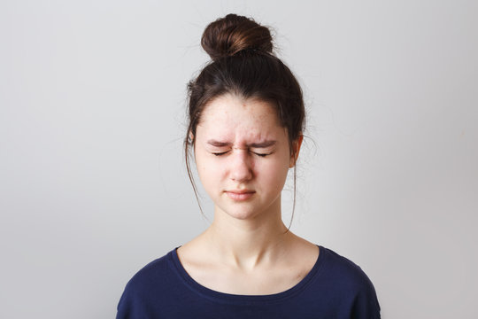 portrait of a pimply teenage girl in a blue T-shirt on a gray background,  with eyes closed