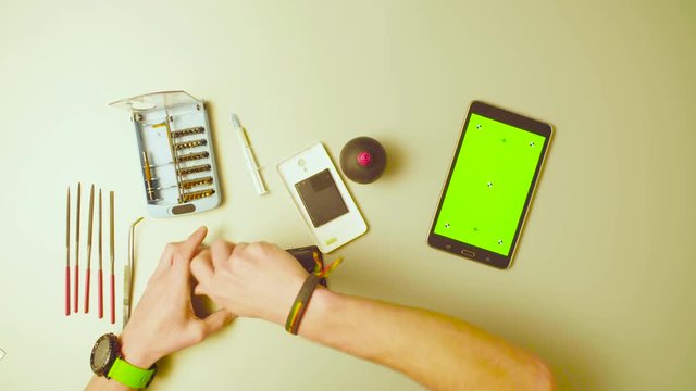 Top view. Green screen. Male hands reparing smartphone and scrolling a tablet with green screen