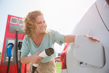 A woman stands at the charging station and holds a plug of the charger for an electric car