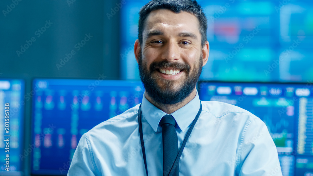 Poster Handsome Stock Market Trader Smiles into the Camera. Behind Him Computer Monitors Showing Ticker Numbers and Graphs.