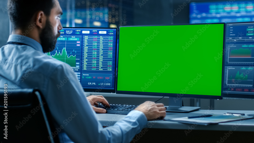 Poster Over the Shoulder View of Stock Market Trader Working on a Computer with Isolated Mock-up Green Screen and Second Display Showing Number Ticker with Graphs.