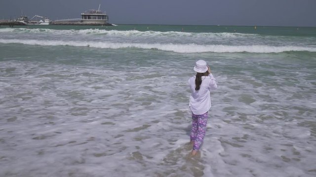 Teenage girl takes pictures of the sea waves of the Persian Gulf on smartphone on the beach of Dubai stock footage video