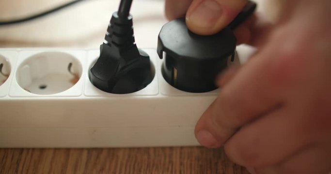 Male hand plugging black power plug into white multiple socket indoors in slow motion. Electricity concept.