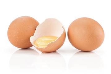 Two brown chicken eggs and one raw yolk in the eggshell half isolated on white background.