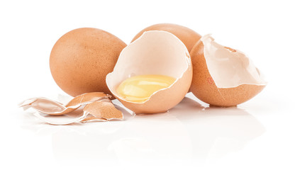 Two brown chicken eggs and one raw yolk in an eggshell half with a lot of cracked pieces isolated on white background.