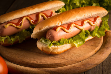Photo of barbecue grilled hot dog with yellow mustard and ketchup on wooden background. Hot dog sandwich with potato fries and sauces.