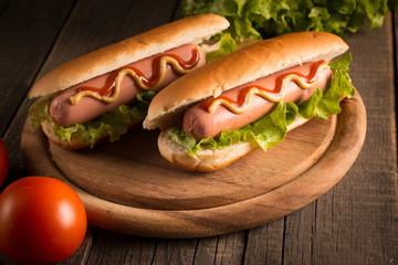 Photo of barbecue grilled hot dog with yellow mustard and ketchup on wooden background. Hot dog sandwich with potato fries and sauces.