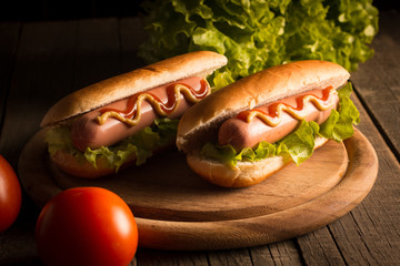 Photo of barbecue grilled hot dog with yellow mustard and ketchup on wooden background. Hot dog sandwich with potato fries and sauces.