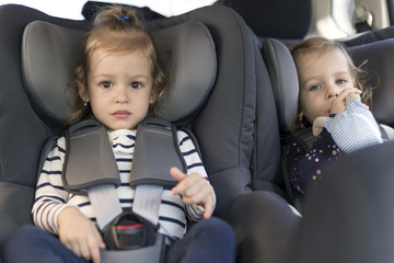 cute small twins in car seats in the car