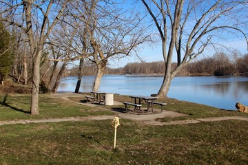 Obraz na płótnie Canvas The empty picnic tables near the flowing river in park.