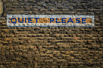 Words Quiet Please painted on a grungy brick wall in block type taken in London. 