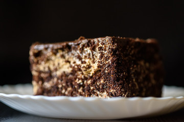 a piece of chocolate cake on a white plate on a dark wooden background. Homemade baking.Close-up view.