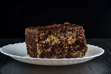 a piece of chocolate cake on a white plate on a dark wooden background. Homemade baking.Close-up view.