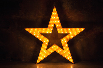 Large wooden star with a large amount of lights in front of dark concrete background. 