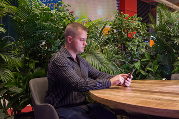 man in a black shirt sitting in a summer cafe and emotionally communicates by phone. It is raining...
