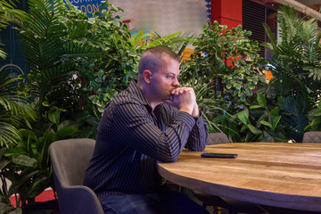 man in a black shirt sitting in a summer cafe and emotionally communicates by phone. It is raining outside.