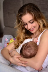 Obraz na płótnie Canvas Breastfeeding baby. Pretty mother holding her newborn child. Mom smile and nursing infant. Beautiful woman and new born love at home. Blondе mother breast feeding baby.
