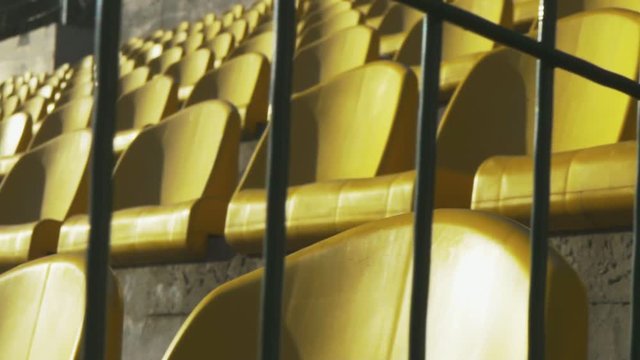 Yellow chairs in an empty stadium behind a metal fence, slow motion 120fps