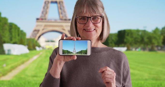 Excited elderly white lady showing off photo she took of Eiffel Tower on phone, Happy Caucasian female tourist showing picture of Eiffel Tower to camera in Paris, France, 4k