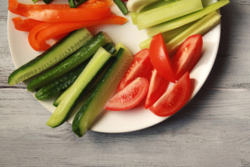 White plate with vegetables for a vegetarian salad. Radishes, tomatoes, celery, bell pepper, onion and cucumber. White wooden kitchen table. Close up. Top view.