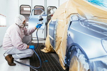 Man with protective clothes and mask painting car using spray compressor. Selective focus. 