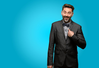 Middle age man, with beard and bow tie happy and surprised cheering expressing wow gesture, pointing with finger