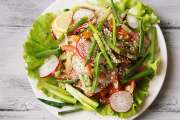 Spring Vegetable Salad on the white plate. Radish, tomato, celery and cucumber. Topped with sesame seeds. Vegetarian dish on the white wooden table. Close up. Top view.