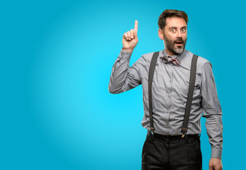 Middle age man, with beard and bow tie happy and surprised cheering expressing wow gesture pointing up