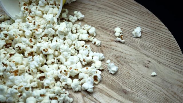 Popcorn in box on black background, close up, rotation wooden table. 4K