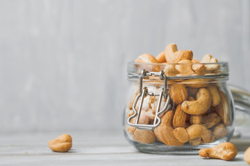 Cashew nuts in an open glass jar over white table against white background. Minimalist food photography style. Copy space.
