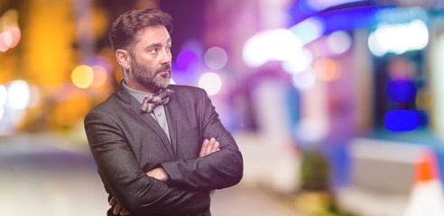 Middle age man, with beard and bow tie with crossed arms confident and happy with a big natural smile laughing at night club