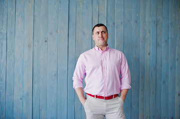 Studio portrait of man in pink shirt against wooden background.