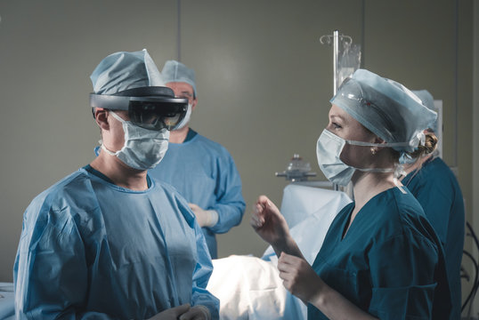 Nurse assisting surgeon with mounting augmented reality holographic hololens glasses before operation