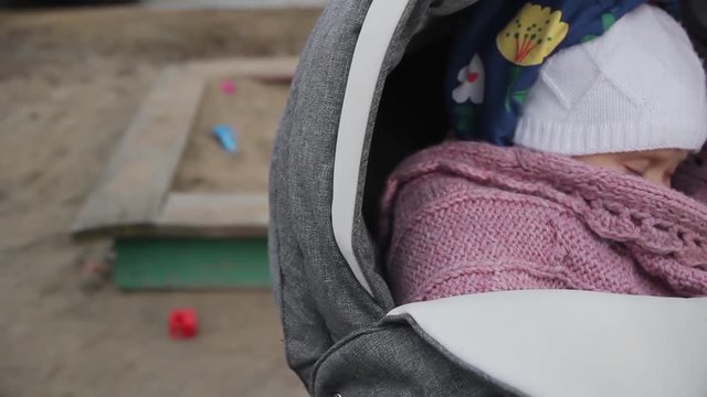 Mother rocking a baby carriage closeup. Sandbox on blurry background