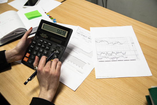 Photo of hands holding the pen and pressing the calculator buttons above the documents