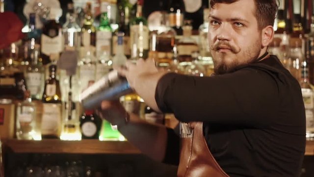 Adult bartender is stirring liquor in a shaker in a bar. He is preparing delicious alcoholic cocktails using special barmans tools
