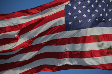 Close Up on American Flag Stars and Stripes Waving against Blue Sky in Afternoon Sun